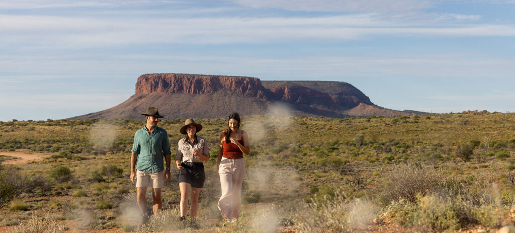 Two ladies walking through the bush with their SEIT Tours Guide and Mount Conner in the background